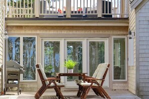 A covered patio with a table and chairs, a grill, and a view of the surrounding trees. - Striking Home with Scenic Marsh Views, Multiple Living Areas, Stroll to Bay (Wellfleet)
