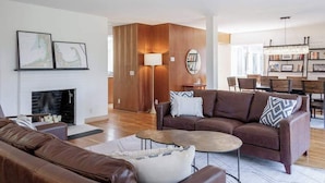 Uma sala de estar moderna com lareira, sofás de couro, uma mesa de centro e um espaço de jantar com cadeiras e um lustre.