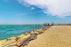 Ein Strand mit einer hölzernen Steg, der ins Meer führt, einer felsigen Küste und einem klaren Himmel.