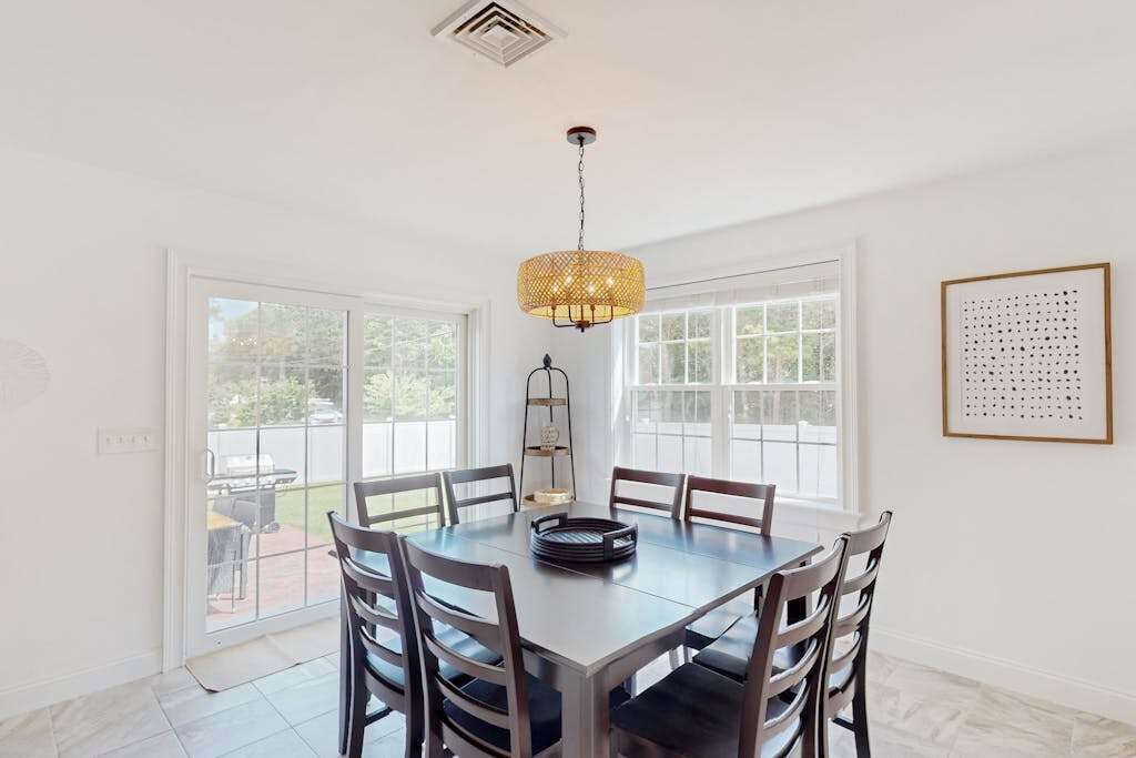 A dining area with a round table, six chairs, a hanging light fixture, and a framed artwork on the wall.