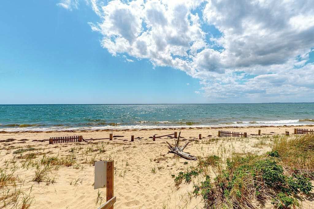 A beach with a wooden fence, a driftwood piece, and a wooden structure on the sand.