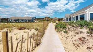 A beachside walkway leading to beachfront properties with a clear sky.