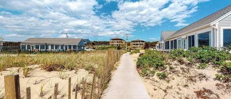 Een kustpad dat leidt naar woningen aan het strand, onder een heldere lucht.
