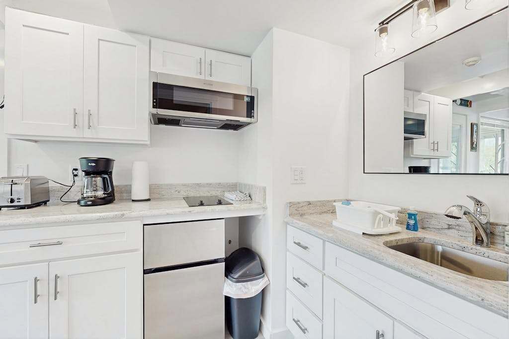 A modern kitchen with white cabinets, a built-in microwave, a coffee maker, and a trash can.