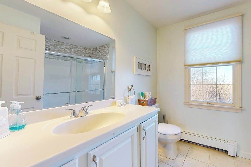 Une salle de bain avec un grand miroir, un lavabo double, des toilettes et une fenêtre avec des stores.