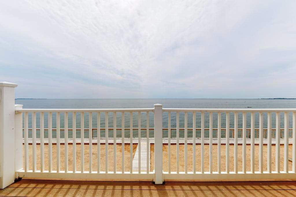 Eine Holzterrasse mit weißer Reling, die auf einen Strand blickt.