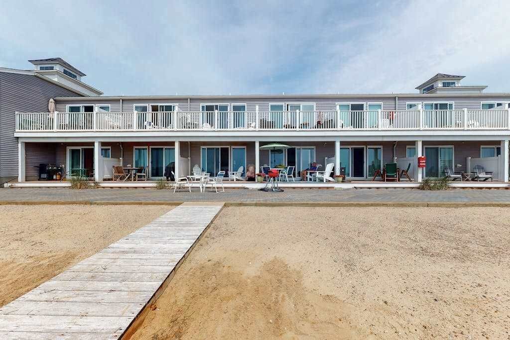 A two-story hotel with balconies, outdoor seating, and a sandy ground area.