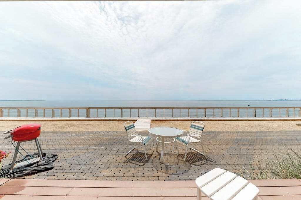 A seaside patio with a round table and chairs, a red chair, and a white chair.