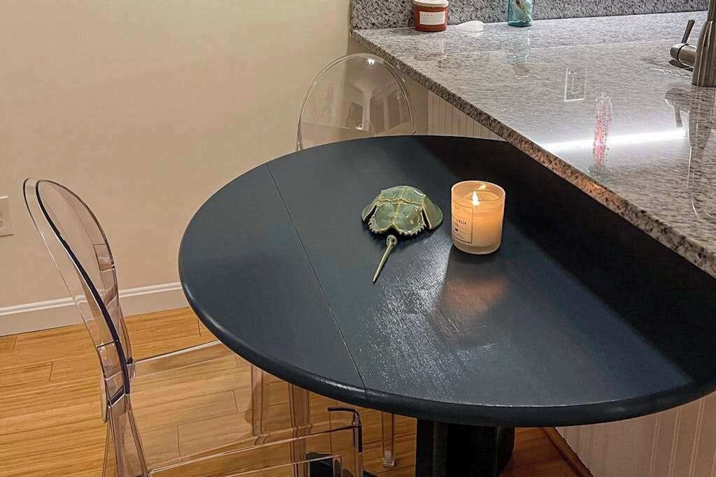 Una mesa redonda con superficie negra, un adorno verde y una vela encendida.