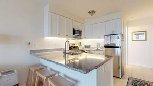 Una cucina moderna con mobili bianchi, un piano di lavoro in granito, un frigorifero in acciaio inossidabile e un forno a microonde integrato.