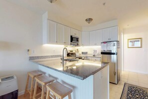 Una cocina moderna con armarios blancos, encimera de granito, refrigerador de acero inoxidable y microondas integrado.