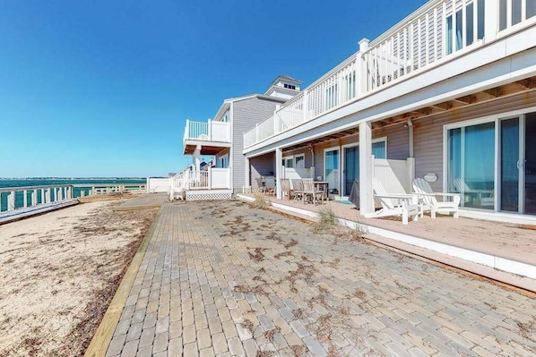 Una propiedad frente a la playa con terraza pavimentada, mobiliario exterior y vista al océano.