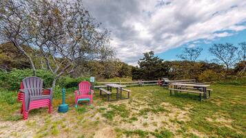 An outdoor seating area with picnic tables and chairs, surrounded by trees and grass.