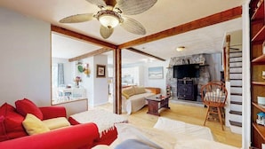 A spacious living room with a red sofa, a white sofa, a wooden coffee table, and a stone fireplace. - Duplex home blocks from Manomet Beach with balcony, firepit & outdoor space (Plymouth)