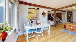 A dining area with a white table and chairs, a vase with flowers, and a wooden ceiling beam. - Duplex home blocks from Manomet Beach with balcony, firepit & outdoor space (Plymouth)