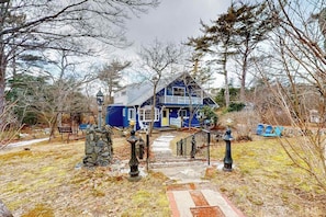 A blue house with a porch, a stone wall, and a pathway leading to the entrance. - Duplex home blocks from Manomet Beach with balcony, firepit & outdoor space (Plymouth)