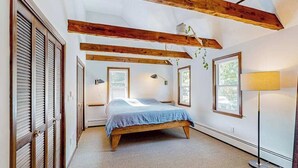 Un dormitorio con cama, vigas de madera, lámpara y ventanas.