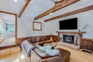 Ein Wohnzimmer mit Ledersofa, Kamin, Fernseher und freiliegenden Holzbalken.
