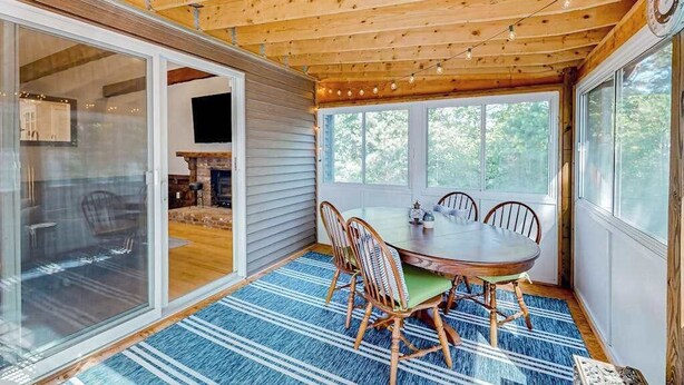 Techo de madera con luces colgantes, una mesa de comedor con sillas y vistas a través de amplios ventanales.
