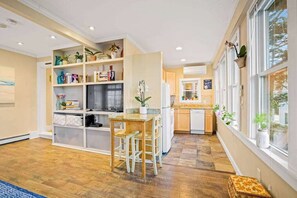 A modern kitchen with built-in appliances, a dining area with a wooden table and chairs, and a window with plants.