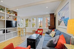 A living room with a sofa, red chairs, a TV, a bookshelf, and a painting.