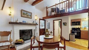 A dining area with a fireplace, wooden furniture, and a kitchen in the background. - The Lodge | Condo in Provincetown with harbor views & two decks (Provincetown)