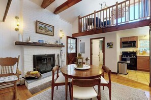 A dining area with a fireplace, wooden furniture, and a kitchen in the background. - The Lodge | Condo in Provincetown with harbor views & two decks (Provincetown)