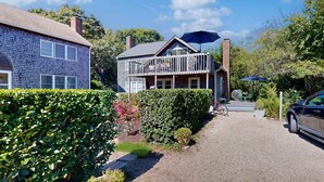A two-story house with a balcony, a gravel driveway, and a car parked in the driveway. - The Lodge | Condo in Provincetown with harbor views & two decks (Provincetown)