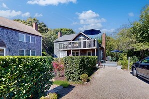 A two-story house with a balcony, a gravel driveway, and a car parked in the driveway. - The Lodge | Condo in Provincetown with harbor views & two decks (Provincetown)
