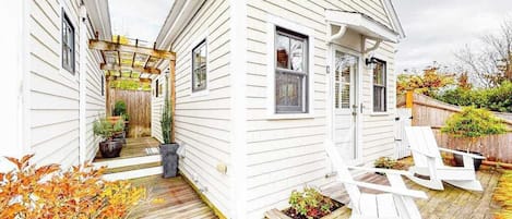 Une maison blanche avec une terrasse en bois, un porche couvert et un petit jardin.