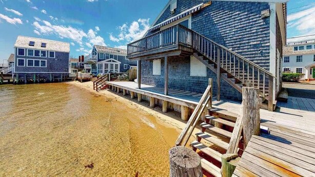 Een pand aan het water met een houten terras, een trap naar een balkon en een glazen gevel.