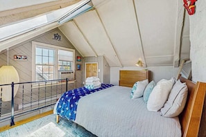 Une chambre avec un plafond en pente, un lit recouvert d’une couvre-lit à motifs bleus et blancs, une tête de lit en bois et une petite table de chevet.