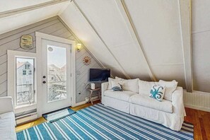 A cozy attic bedroom with a white sofa, a television, and a view of the city through a door.