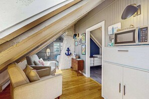 A loft-style room with a wooden ceiling, a white cabinet with a microwave, a sofa, and a dresser.
