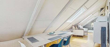A modern loft-style room with a high ceiling, a dining table with chairs, a sofa, and a television.