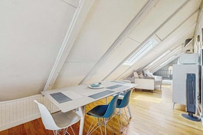 A modern loft-style room with a high ceiling, a dining table with chairs, a sofa, and a television.