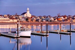 Ein Yachthafen am Wasser mit vertäuten Booten, eine markante Kirche mit Kirchturm und Wohngebäude entlang der Küste.