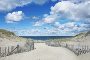 A sandy beach path leading to the ocean, with a wooden fence on either side. - Pristine cottage with charming screened porch & balcony - steps to the Boatslip (Provincetown)