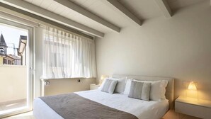 Una camera da letto con un letto, comodini, una finestra con tende e vista sugli edifici.