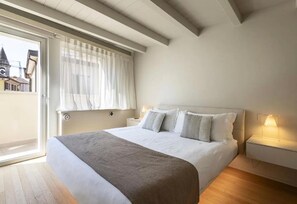 A bedroom with a bed, bedside tables, a window with curtains, and a view of buildings outside. - Apartment 'Palazzo Cordigero - Fortezza' with Lake View and Wi-Fi (Peschiera del Garda)