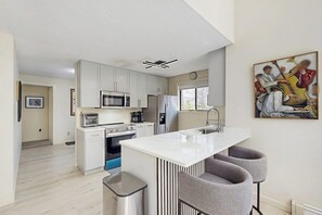 A modern kitchen with white cabinets, a central island with bar stools, a microwave, and a refrigerator. - Spacious island home near Farm Neck Golf Course, the beach and town (Oak Bluffs)