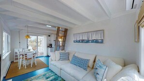 Ein modernes Wohnzimmer mit einem weißen Sofa, einem Essbereich mit weißem Tisch und Stühlen sowie einem großen Fenster.
