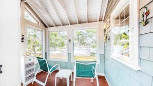 Eine überdachte Veranda mit Holzboden, zwei grüne Stühle, einem kleinen Tisch und einem weißen Schrank.