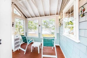 A covered porch with a wooden floor, two green chairs, a small table, and a white cabinet.