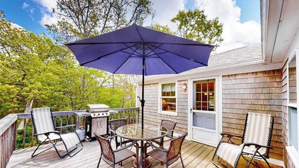 En træterrasse med grill, et rundt bord med stole og en stor parasol.