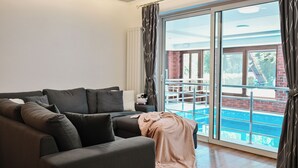 En moderne stue med en mørk sofa, et tæppe og udsigt til en swimmingpool gennem store glasdøre.
