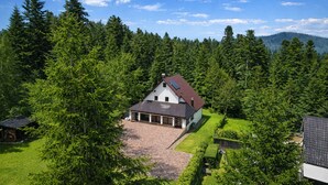Et hus omgivet af tæt skov, med en belagt indkørsel, der fører til indgangen.