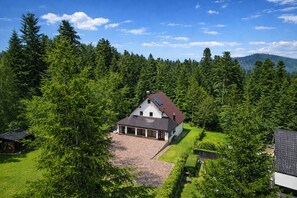Ein Haus, umgeben von dichtem Wald, mit einer gepflasterten Auffahrt zum Eingang.