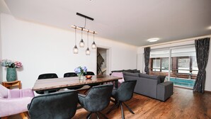 En moderne stue med spiseområde, med et træbord, sorte stole, en grå sofa og et stort vindue med gardiner.
