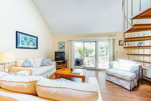 A living room with a sofa, ottoman, coffee table, TV, and artwork on the wall.